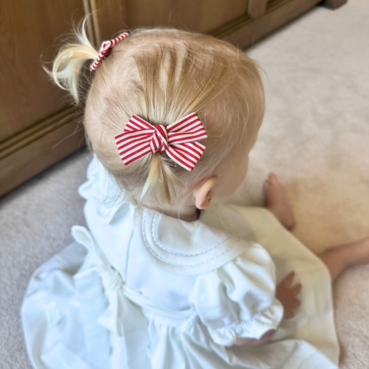 Girl wearing the Red Stripe Micro Pigtail Set, featuring two clips with playful red stripes. This festive accessory is perfect for holiday hairstyles, adding charm to her pigtails and ponytails. Ideal for toddlers and girls, these clips enhance any look with a touch of Christmas.