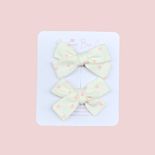 Kids pigtail hair bow set in white with pink hearts, charming and perfect for adding a sweet touch to hairstyles.