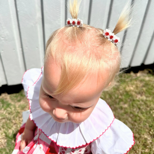 Toddler wearing the Red Daisies Clip Set, featuring two delicate red daisy designs. Each clip measures about 3.5 cm, adding a charming pop of color to her hairstyle. Ideal for everyday wear or special occasions, these clips offer a sweet and playful accent to any outfit.